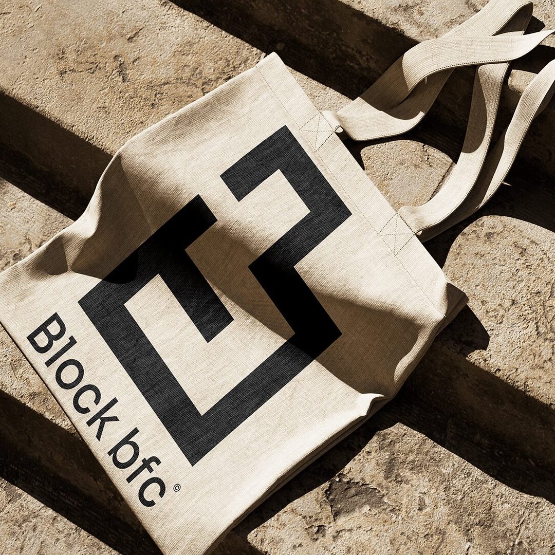 Mockup tote bag en toile naturelle avec le logo BlockBFC brôdé en noir, posé sur une surface en pierre. Application des visuels géométriques du projet de branding BlockBFC