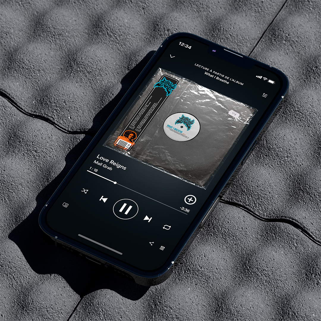 iPhone posant sur béton, écran affichant « Love Reigns » de Mall Grab sur player audio avec la cover vinyle What I Breathe